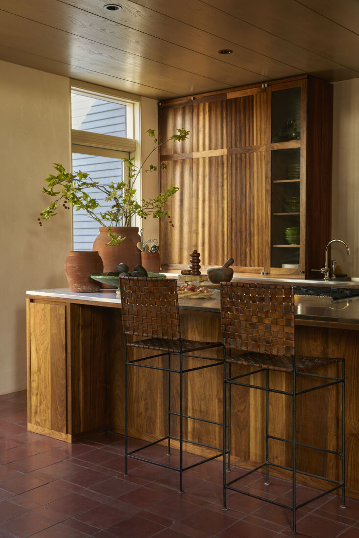 A kitchen featuring black walnut cabinetry, red tile flooring, and woven leather stools.