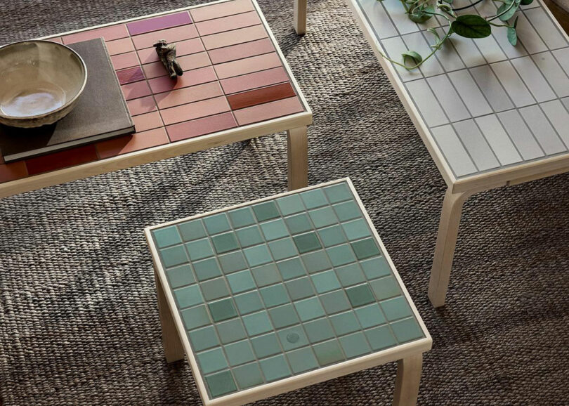 Three square Artek x Heath tables in red, cream, and green arranged together on a rug.