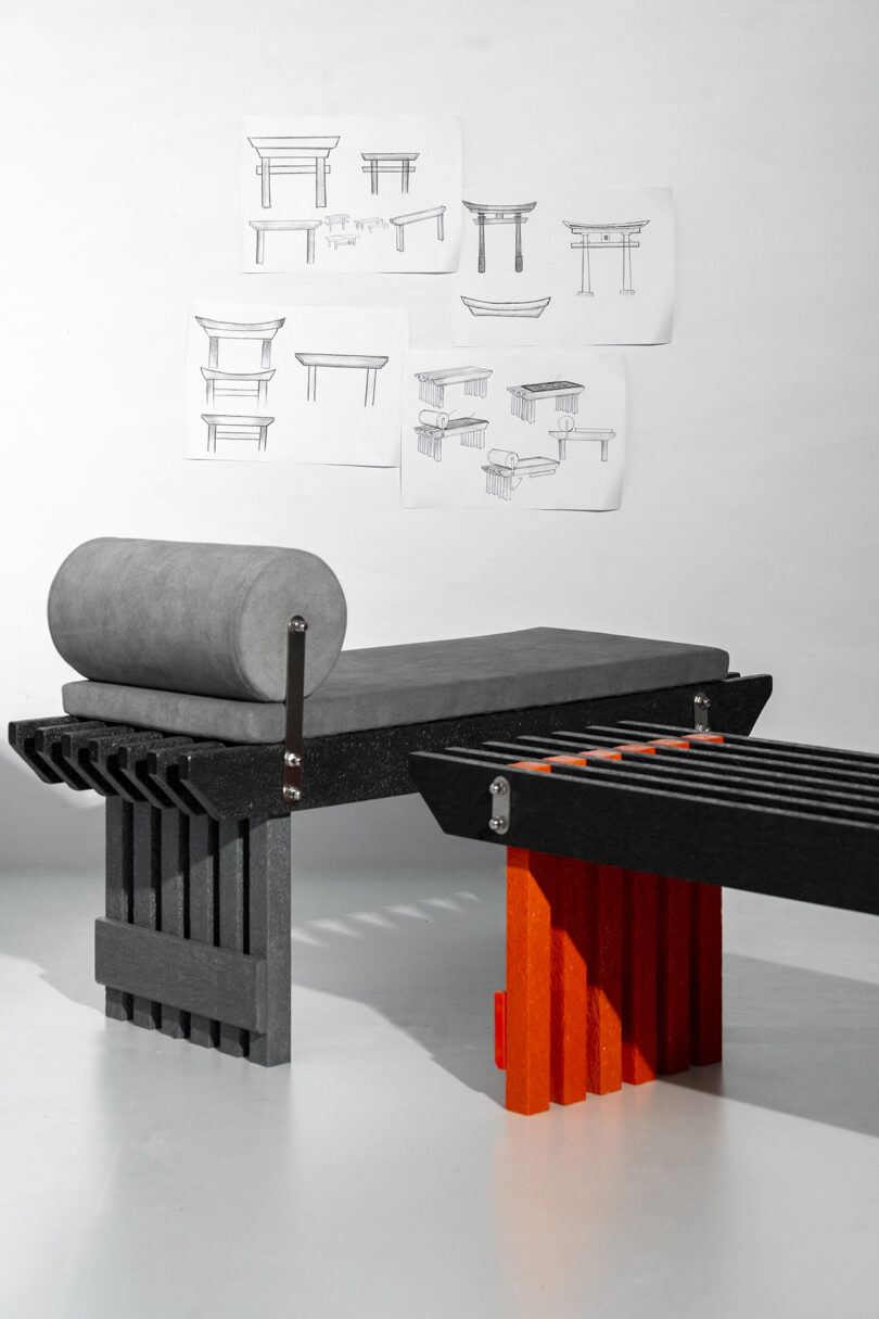 A modern bench with a grey cushion positioned in front of design sketches on a wall.