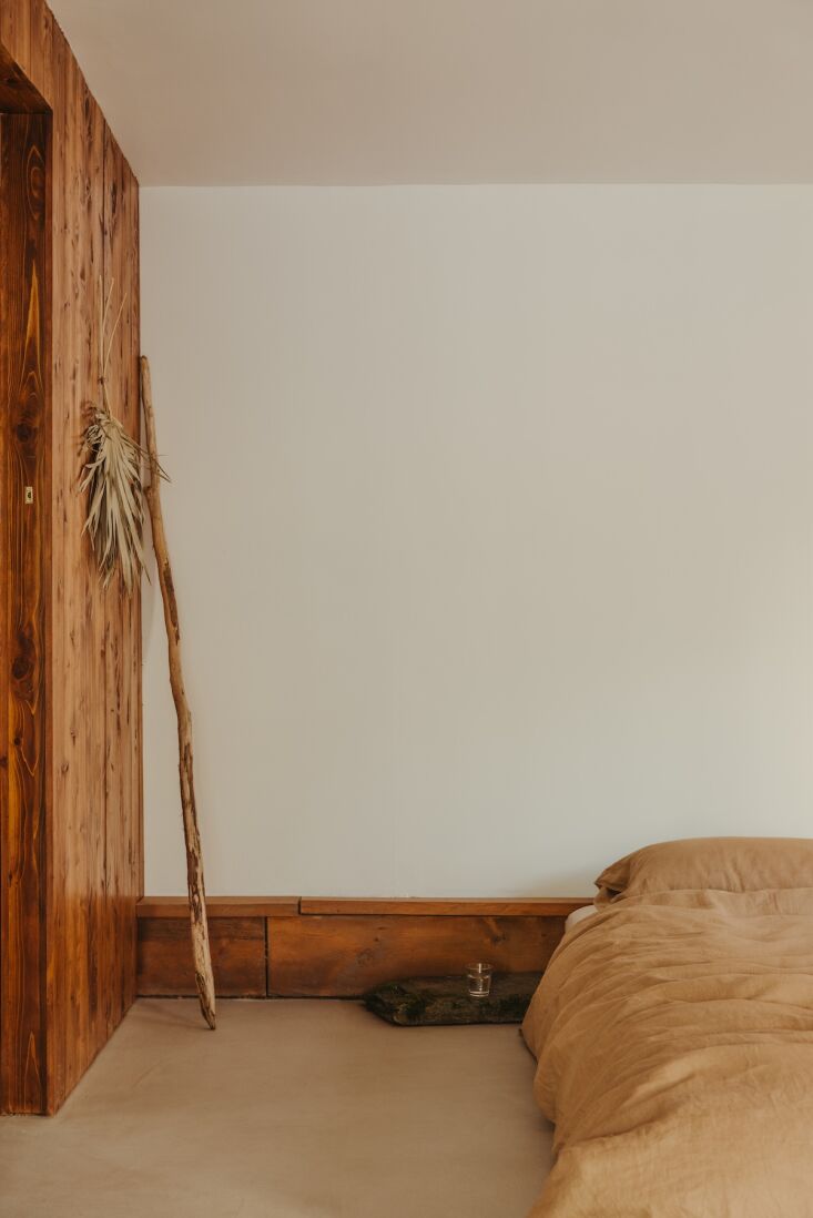 A low-profile wooden bed frame in a minimalist bedroom with a large window.