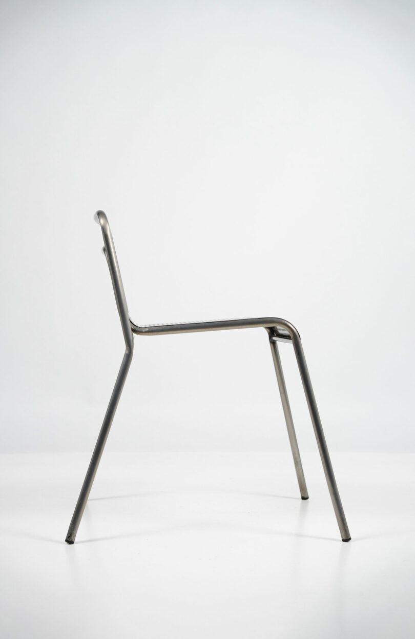 Side profile of a minimalist steel chair with a tubular frame and thin silhouette.