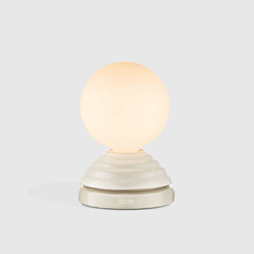 A white spherical sunrise clock on a textured base displaying 07:00 AM.