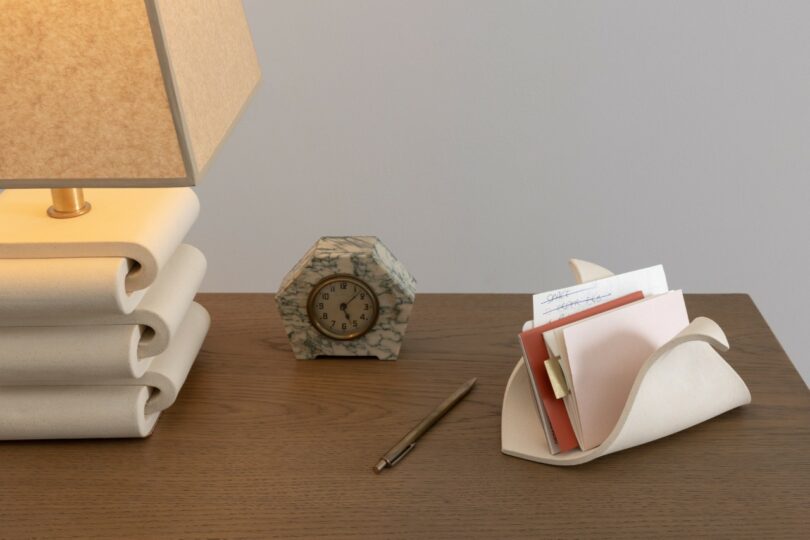 A sculptural ceramic holder containing a pink notepad and papers on a wooden desk.
