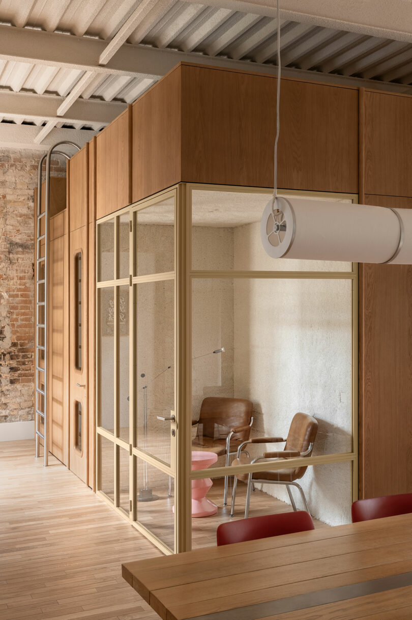 A small glass-walled meeting room with leather chairs and a metal ladder, showcasing a 'Tram' design influence.
