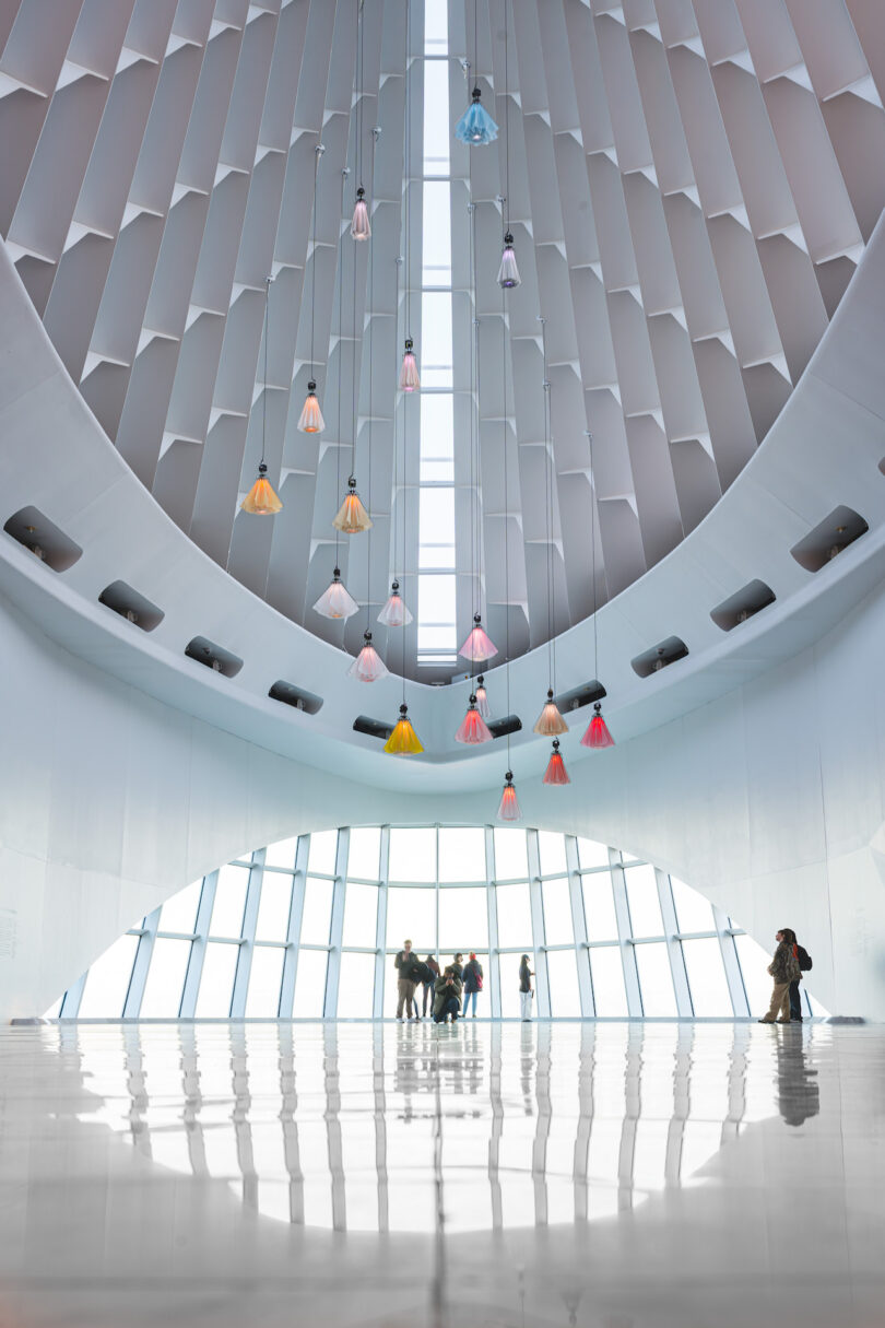 The high-ceilinged Windhover Hall at the Milwaukee Art Museum featuring colorful hanging kinetic flowers and visitors.