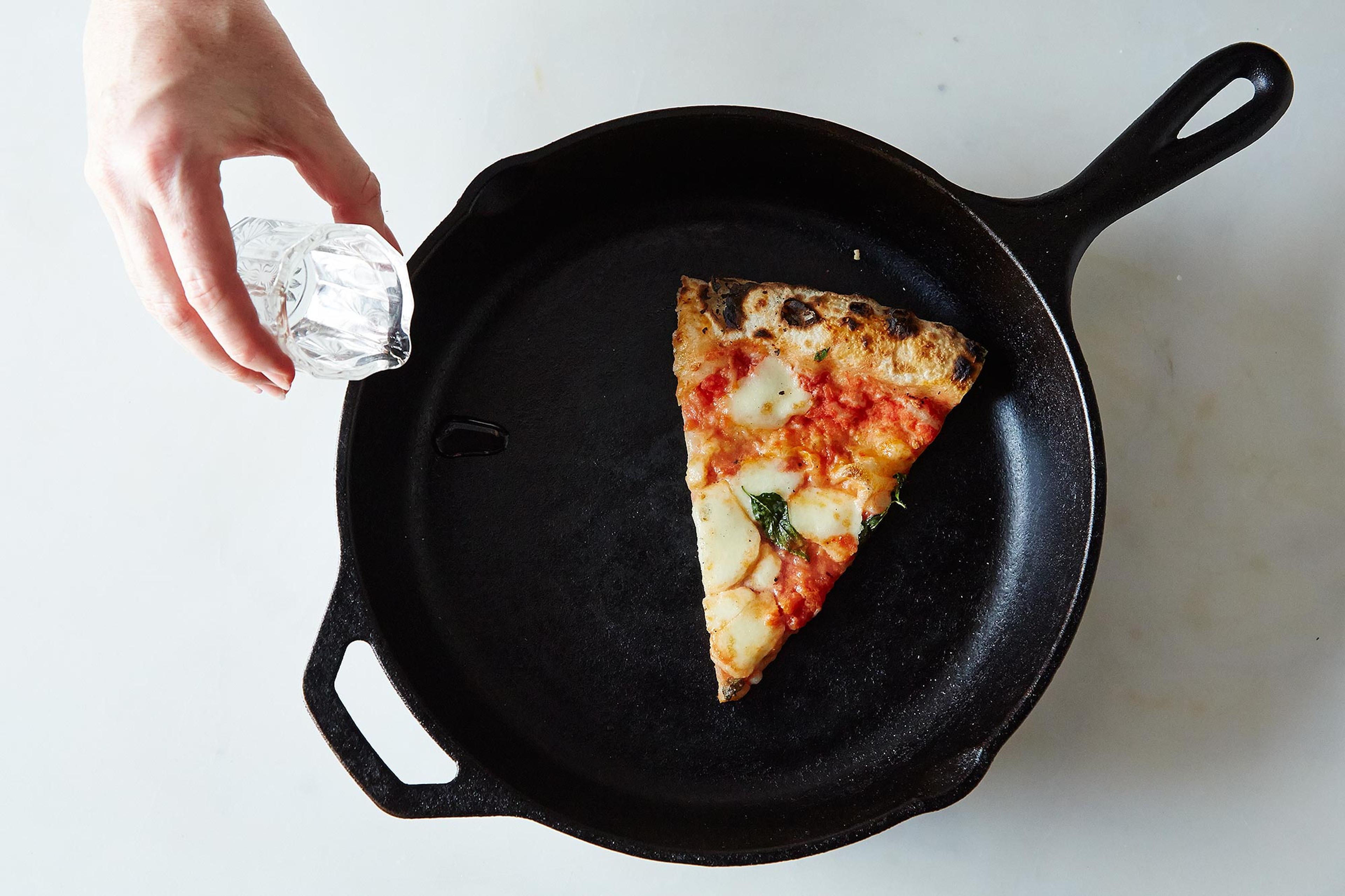 Slices of leftover pizza being reheated in a black cast-iron skillet on a stovetop.