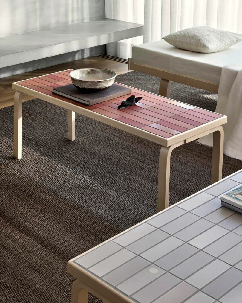 A rectangular red-tiled Artek coffee table styled with a book and sculpture in a contemporary living room.