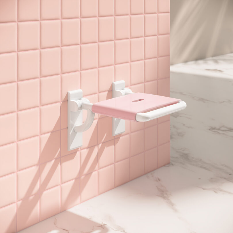 A pink foldable wall seat mounted on pink square tiles next to a marble surface.