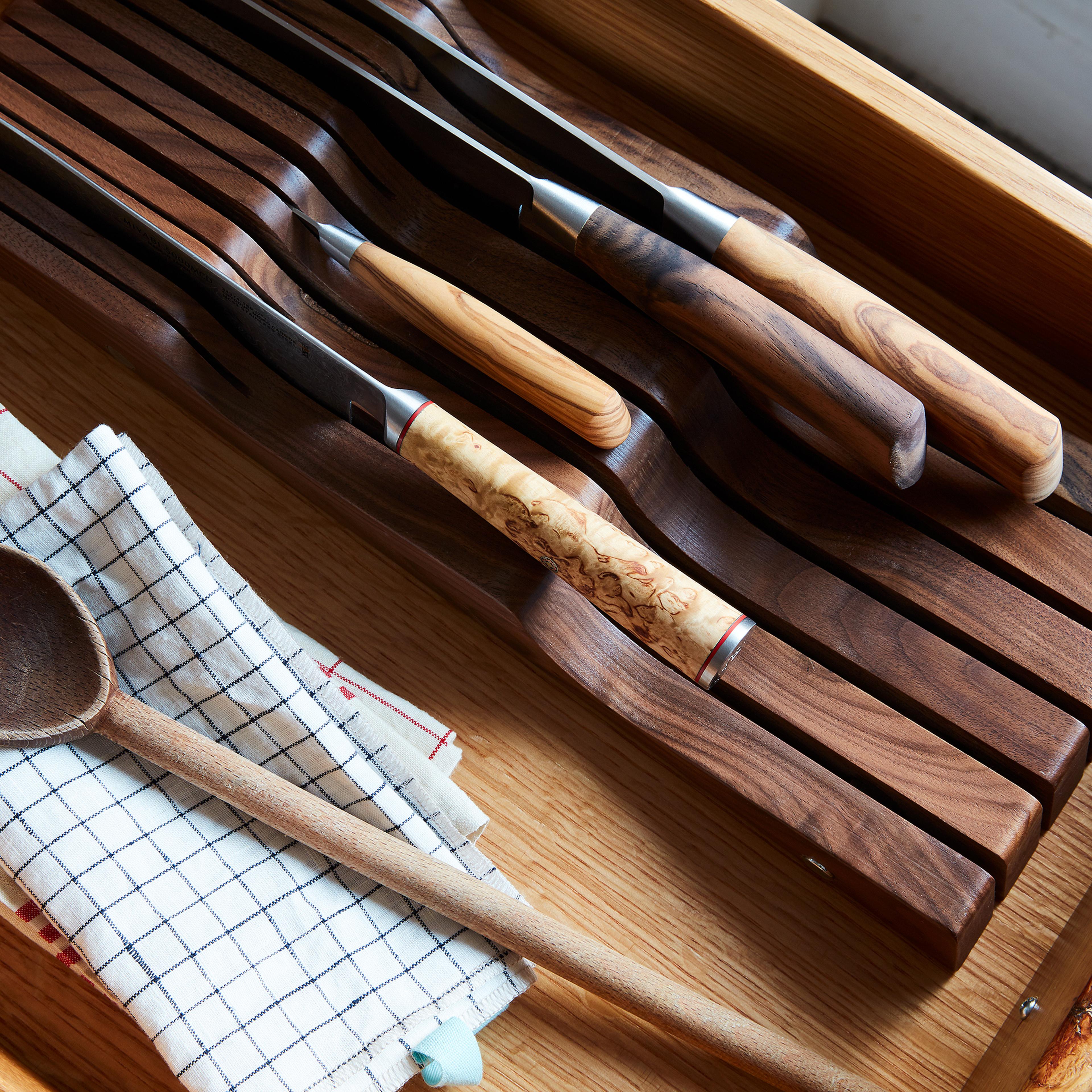 A wooden knife organizer fitted inside a kitchen drawer holding various kitchen knives.