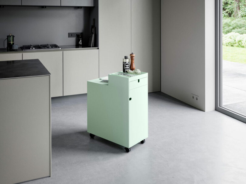 A mint green NEXT trolley used for spice and utensil storage in a minimalist kitchen.