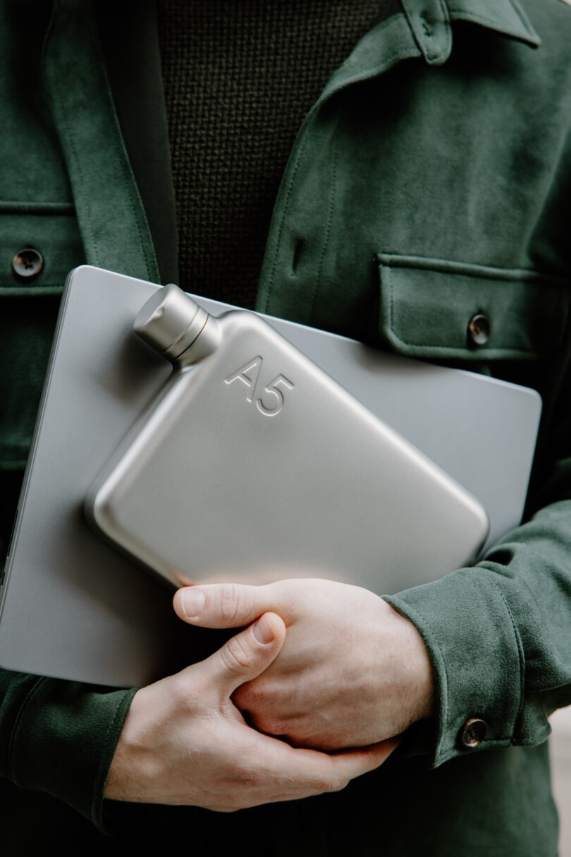 A person holding a silver A5 memobottle and a laptop, emphasizing its slim profile.