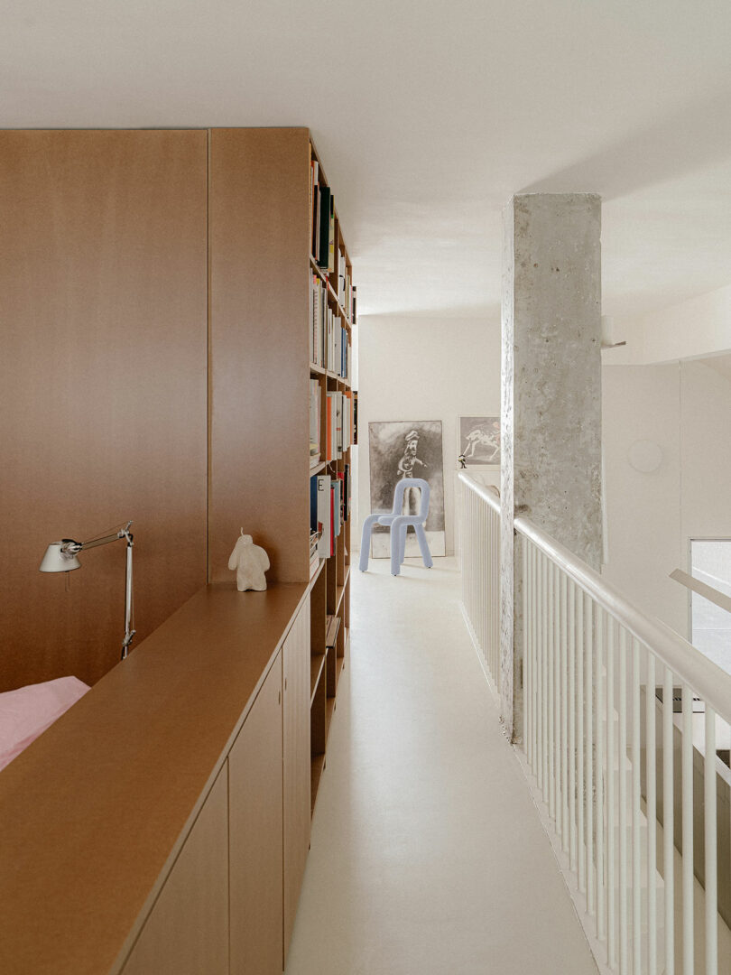A clean hallway with wooden bookshelves and a desk lamp leading to a bright room.