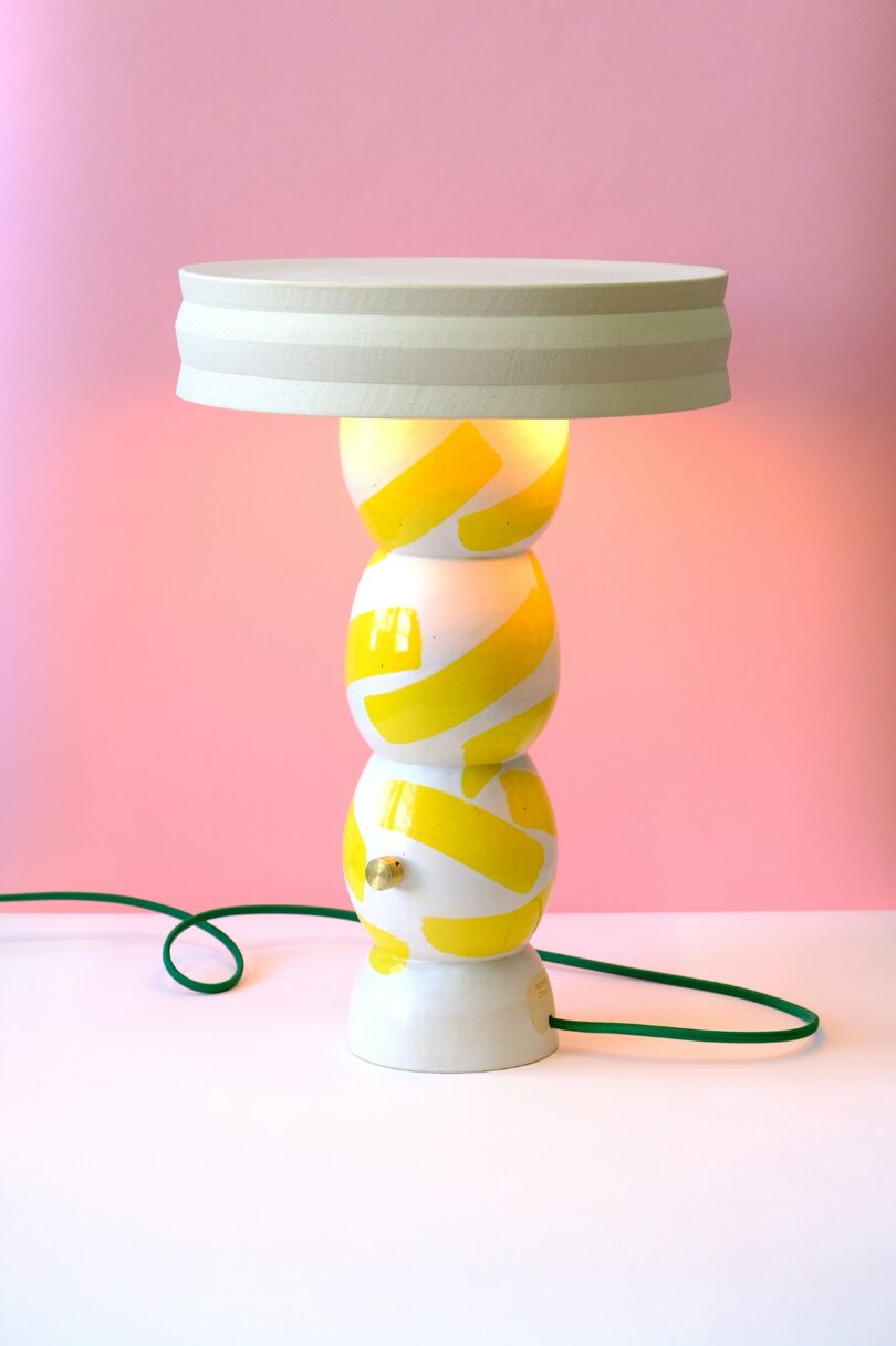 A white and yellow striped ceramic lamp on a bright pink background.