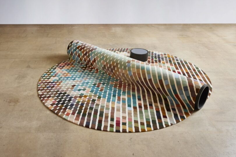 A modular bench-carpet hybrid furniture piece with a small side table in a bright room.
