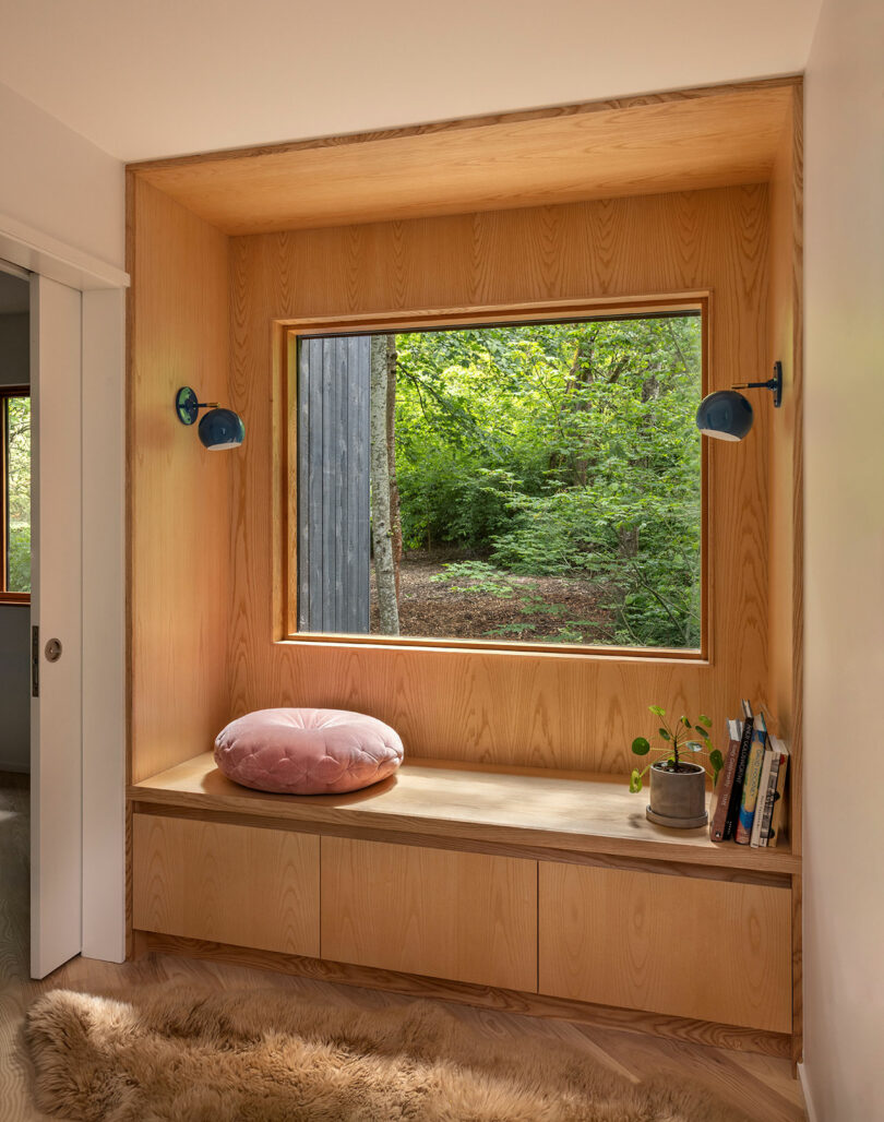 A built-in wooden window seat with a view of a green forest and blue wall accents.