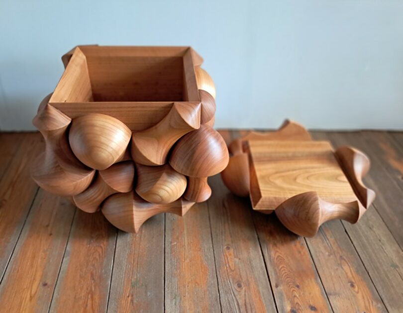 The Illusion Box shown open with its carved lid resting beside the main storage compartment on a wooden floor.