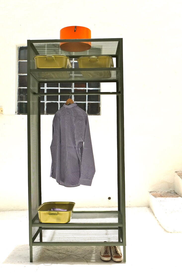 A black wrought iron armoire with built-in shelves containing white enamelware storage trays.