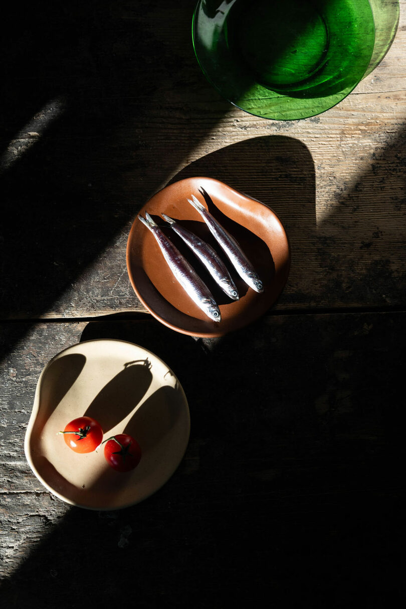 Simple food served on ceramic plates on a rustic table with strong sunlight and shadows.
