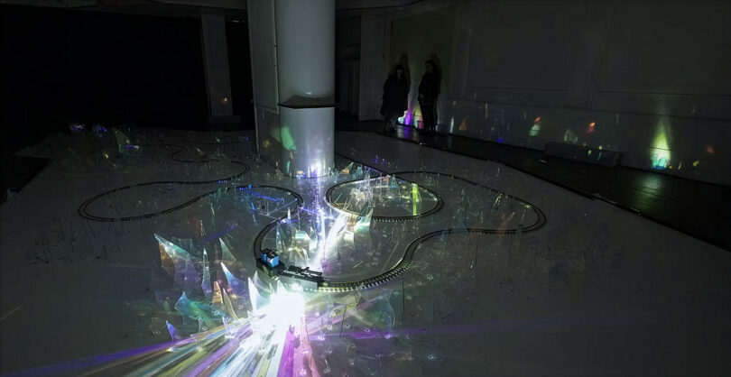 An immersive dark room featuring circular tracks and glowing crystal-like structures reflecting colorful light.