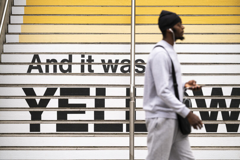 A pedestrian walks past a step featuring a large Pantone-style layout and the text 'And it was YELLOW.'