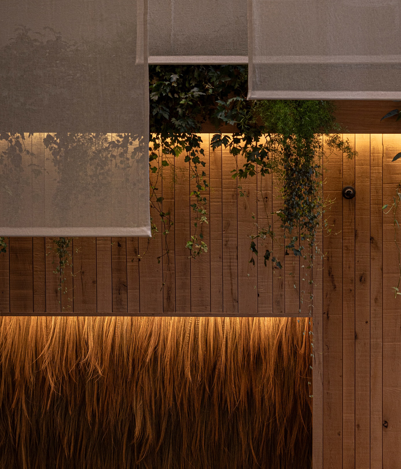 Interior view of a wooden wall with integrated lighting and lush hanging greenery under a mesh ceiling.