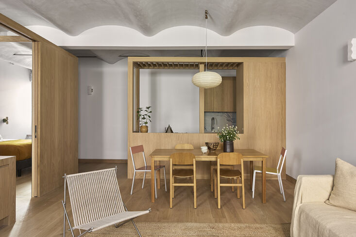 Custom white oak cabinetry and millwork volumes defining the entry and kitchen areas of a small apartment.
