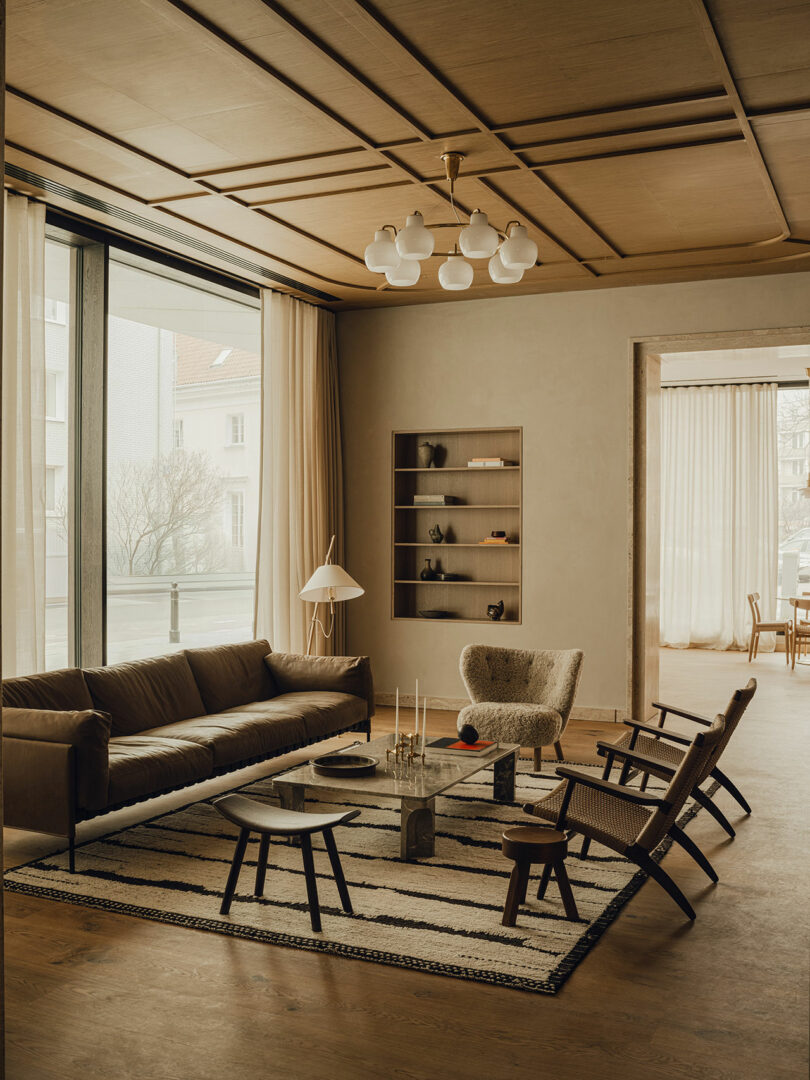 A modern hotel lounge featuring a brown leather sofa, marble coffee table, and large windows with sheer curtains.