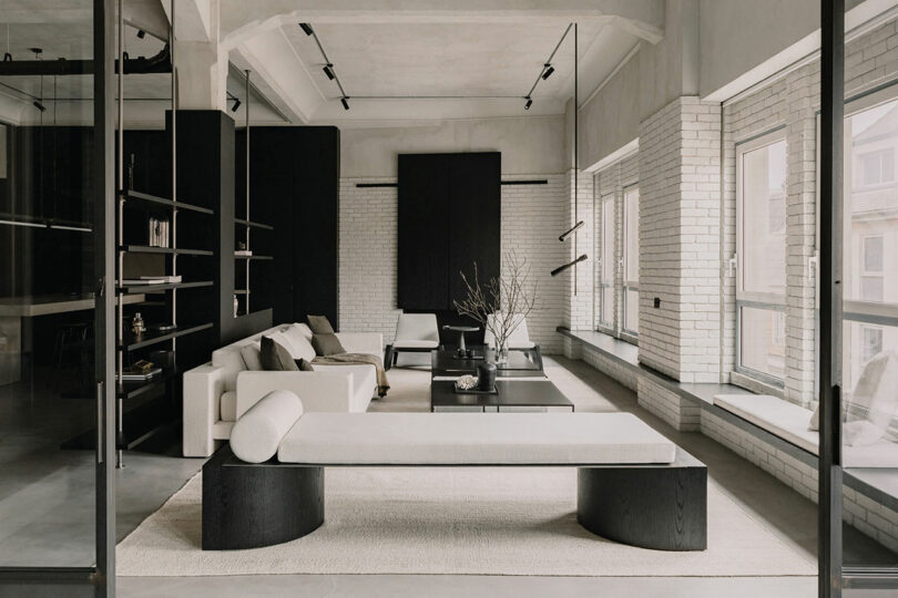 A modern living room with exposed brick, large windows, and neutral-toned minimalist furniture.