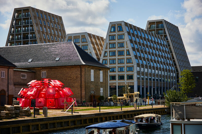 A wide shot of the Copenhagen canal featuring modern glass buildings and the red sculptural installation.