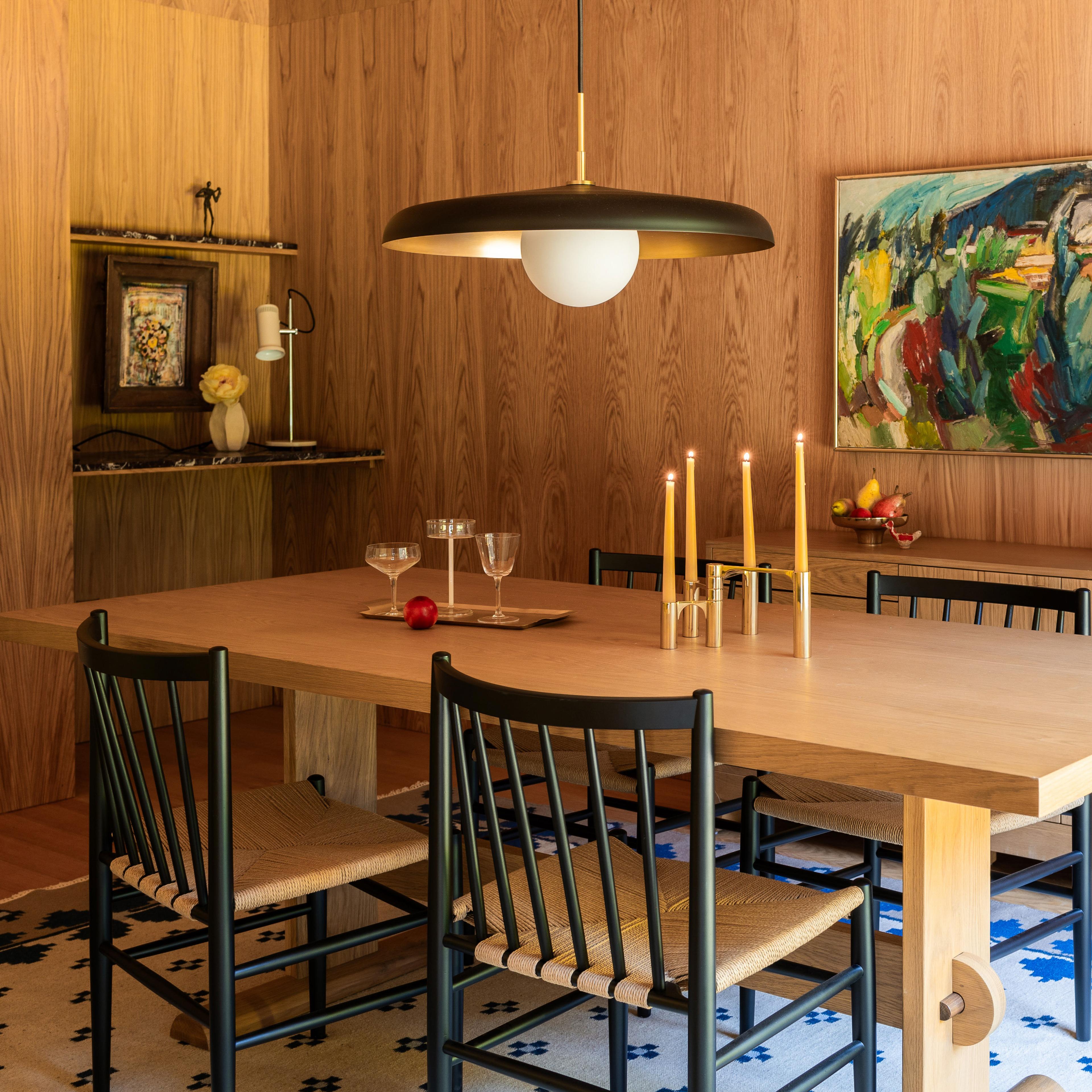 A dining room featuring vertical wooden wall panels and a black and brass pendant light.