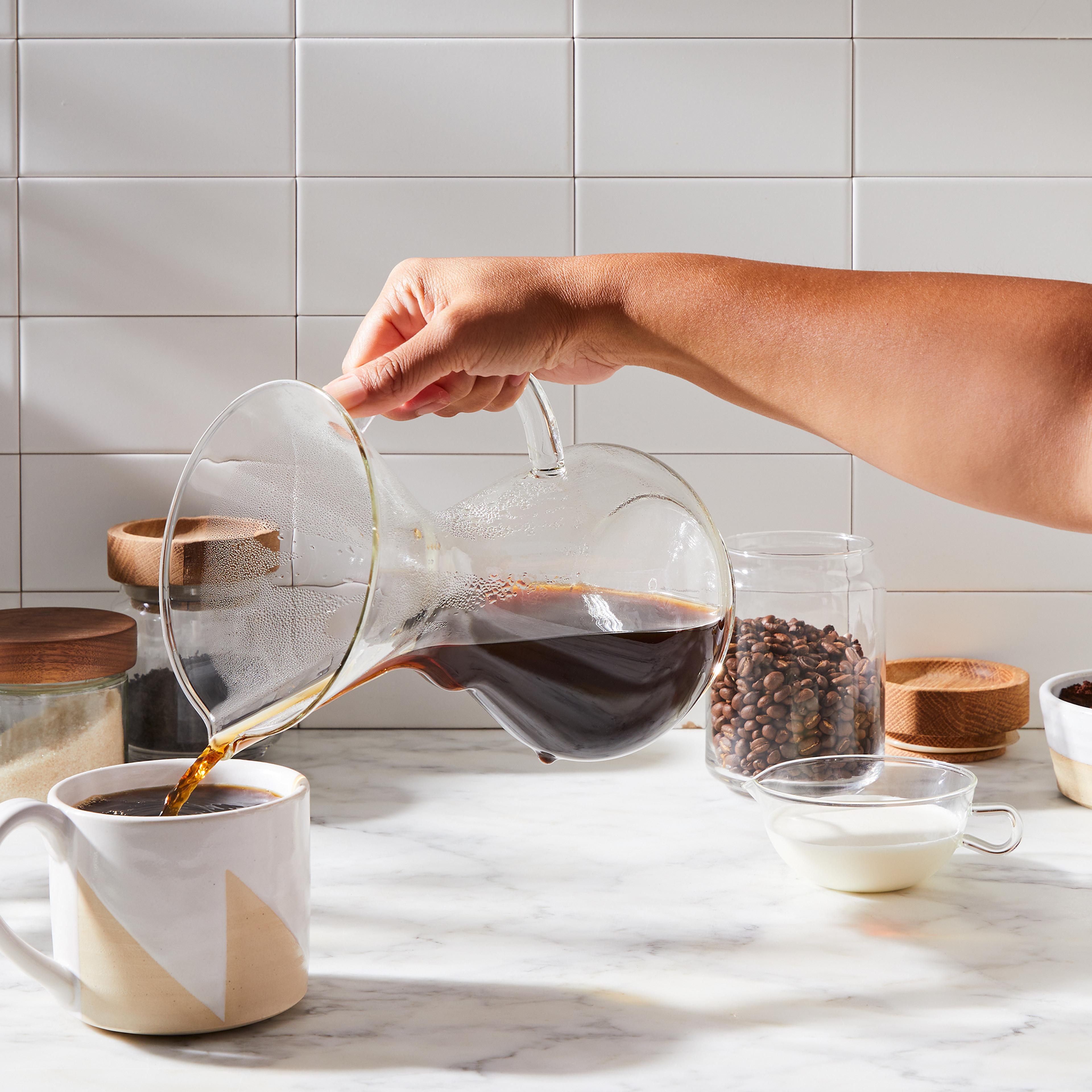 A minimalist Chemex pour-over glass coffee maker sitting on a clean, empty countertop.