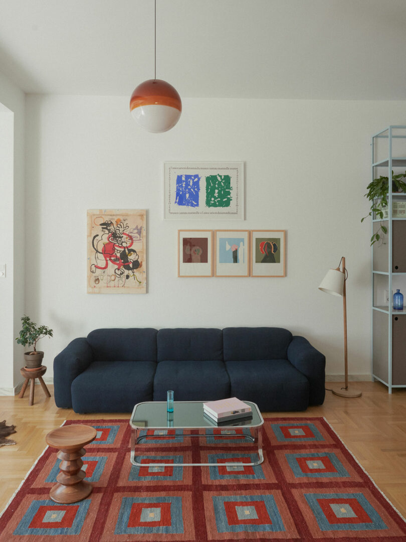 Living room with a dark blue sofa, geometric rug, and framed art against neutral walls.