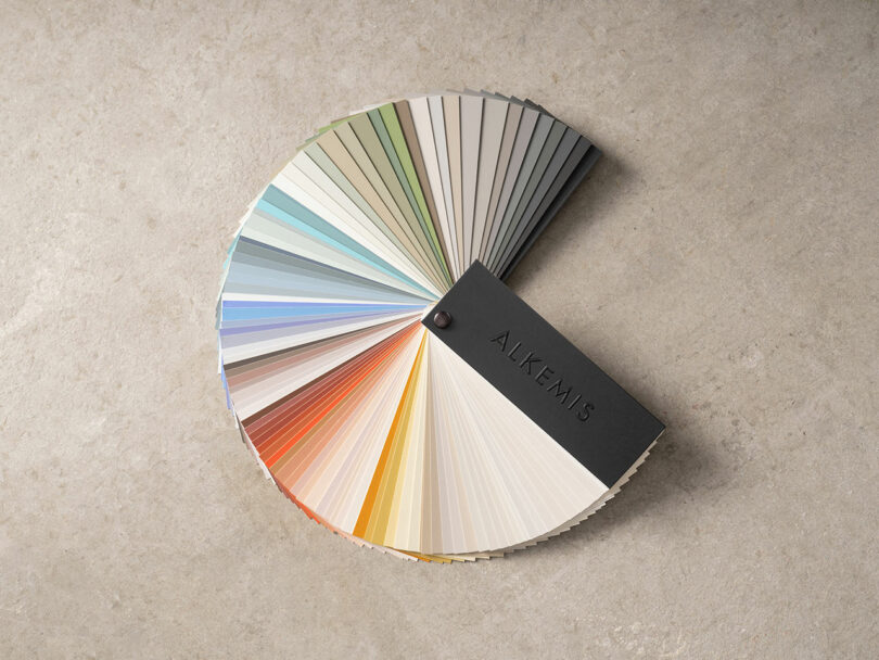 A fan of Alkemis color swatches arranged on a stone surface.