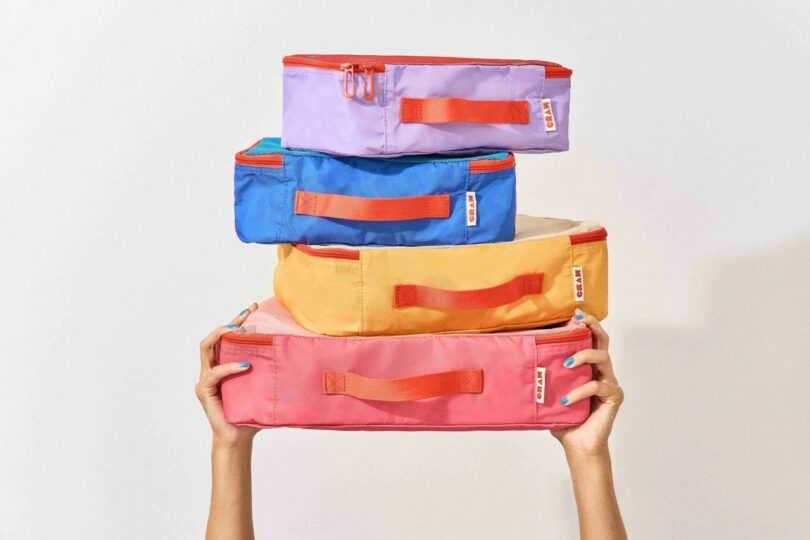 A set of four brightly colored fabric packing cubes in pink, yellow, blue, and purple.