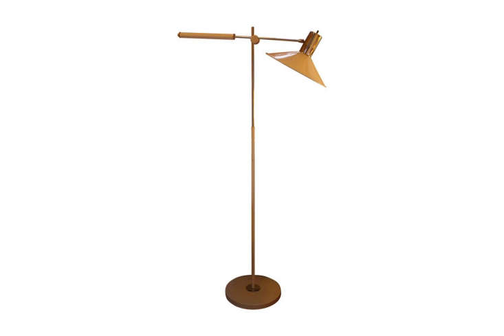 A vintage brass swing-arm floor lamp next to a bed.