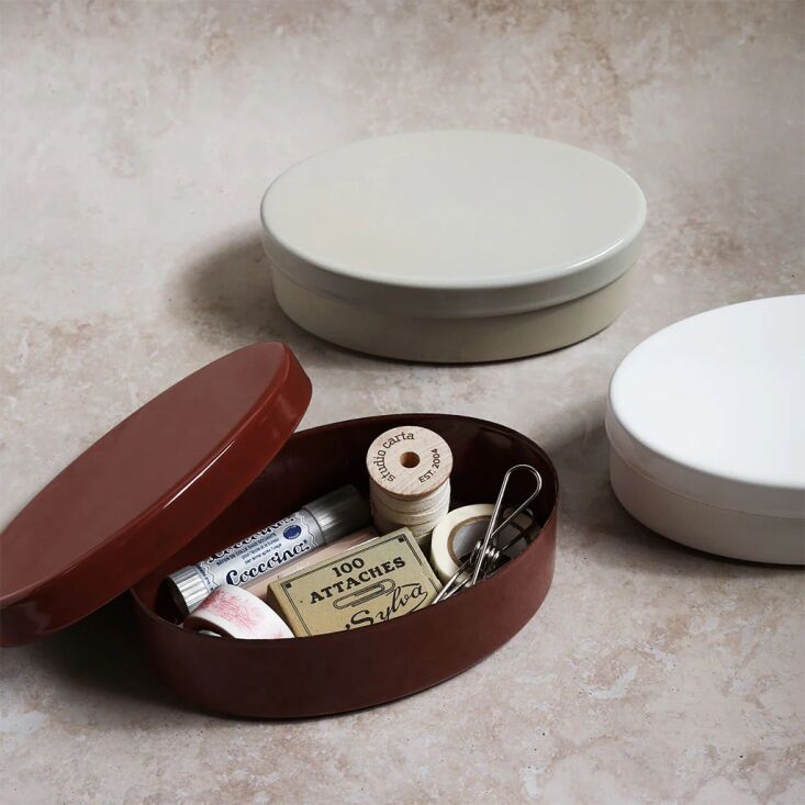An enamel bento box filled with office supplies like washi tape and pens.