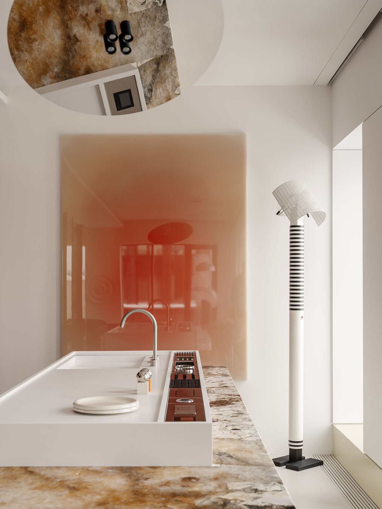 Close-up of a marble countertop and integrated stove against a reflective red wall panel.