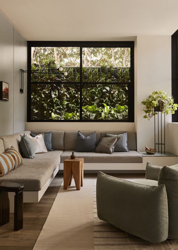 A massive wrap-around built-in sofa facing a large floor-to-ceiling window overlooking a garden.