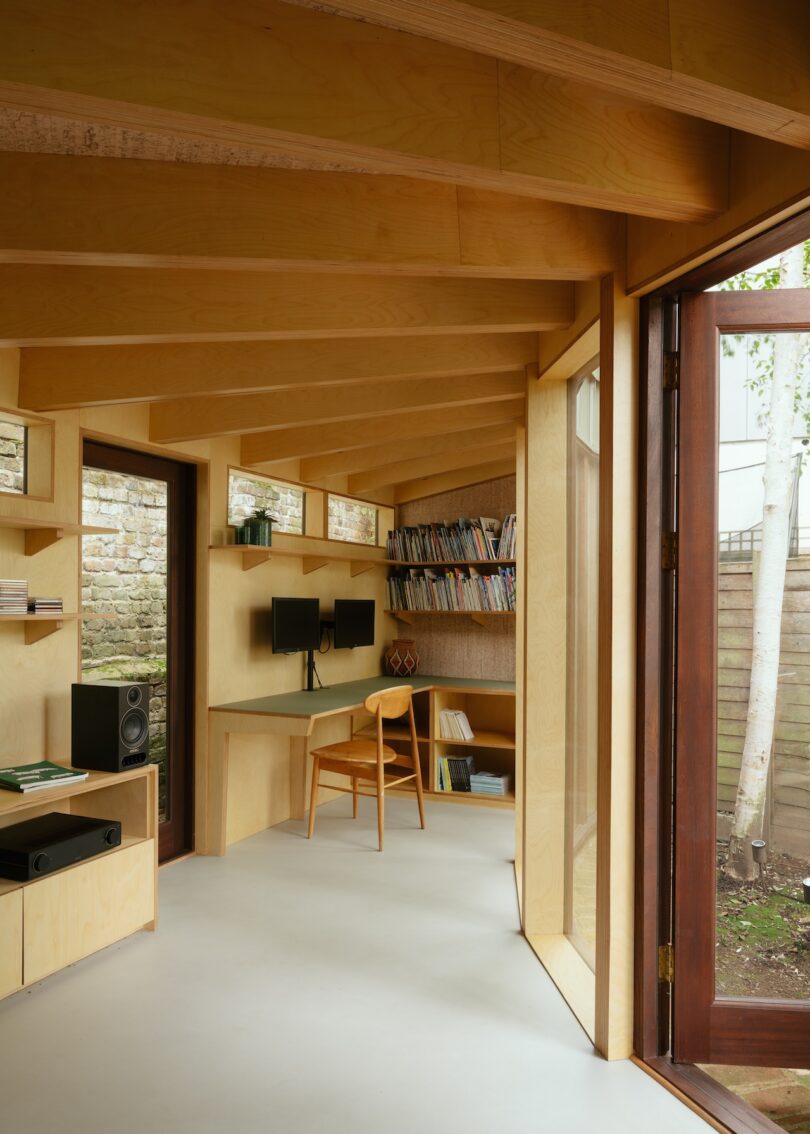View from a modern wooden office through an open door looking out at birch trees in a fenced yard.
