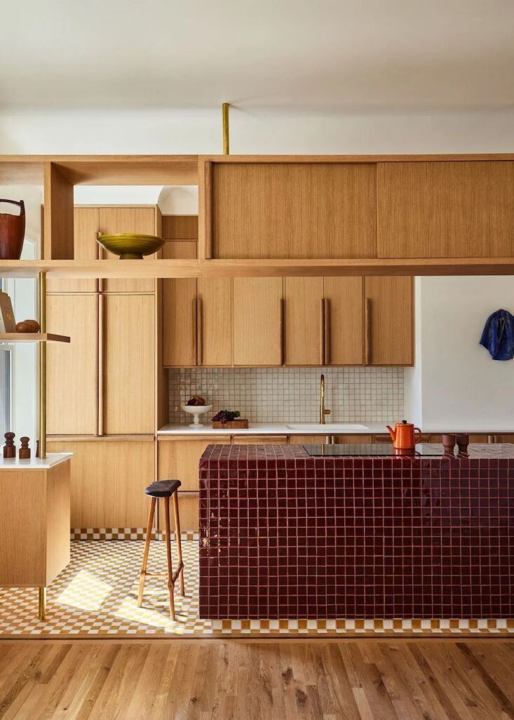 A kitchen island wrapped in glossy deep red square tiles with dusty rose grout.