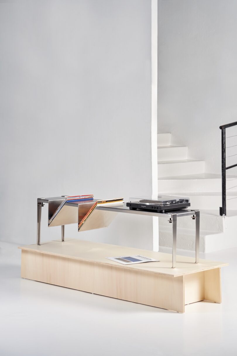 Minimalist wooden bench with Tiptoe legs and a built-in metal V-shaped record rack.