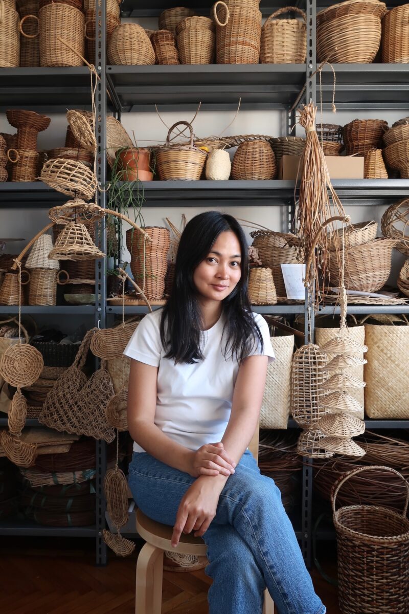 A woman surrounded by various woven wicker baskets and artisan crafts.