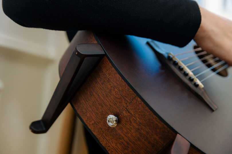 Close-up of a person's arm resting on the polished wooden body of an acoustic guitar.