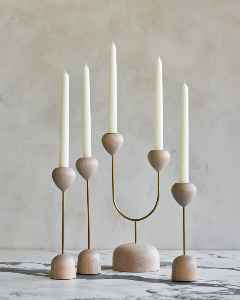 Four minimalist light wood candle holders with white tapers.