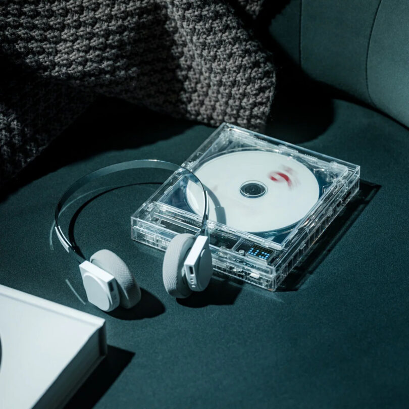Modern headphones and a transparent CD player resting on green fabric.