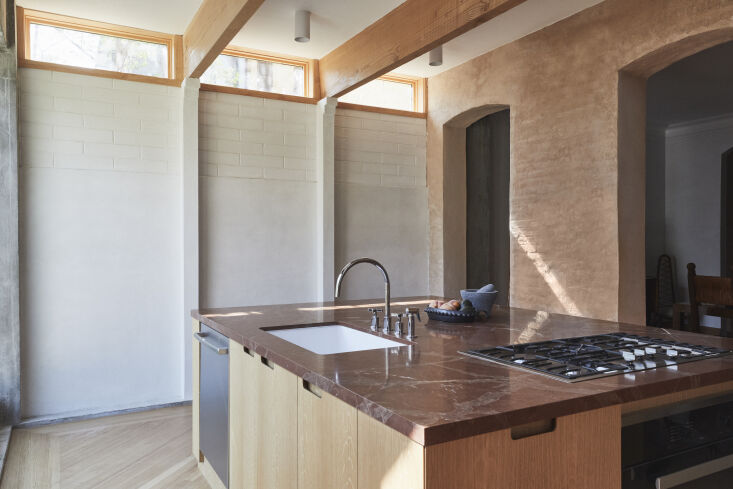 Modern kitchen in a townhouse extension featuring a large red stone island and Douglas fir ceiling beams.