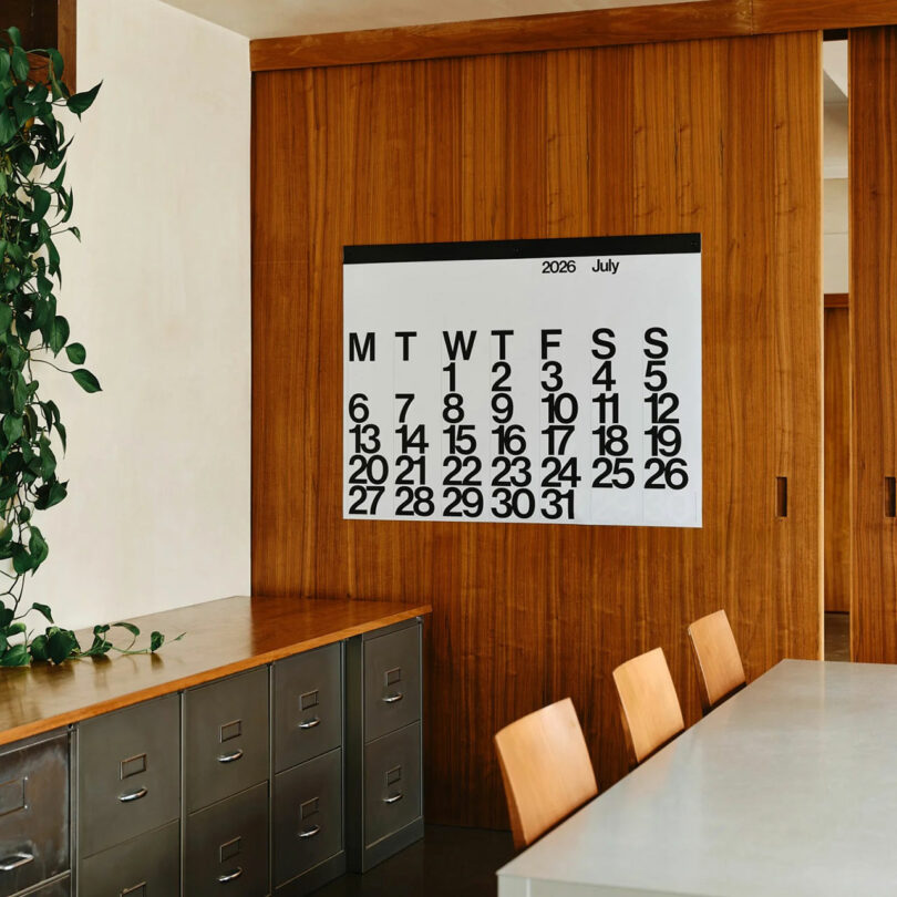 A large 2026 wall calendar hanging in a bright, modern office space above a conference table.
