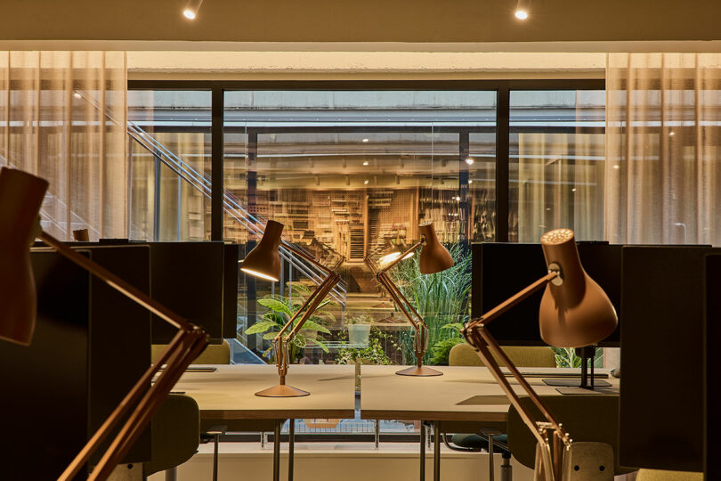 A bright office workstation with a desk lamp facing a large window that opens onto a lush green courtyard.