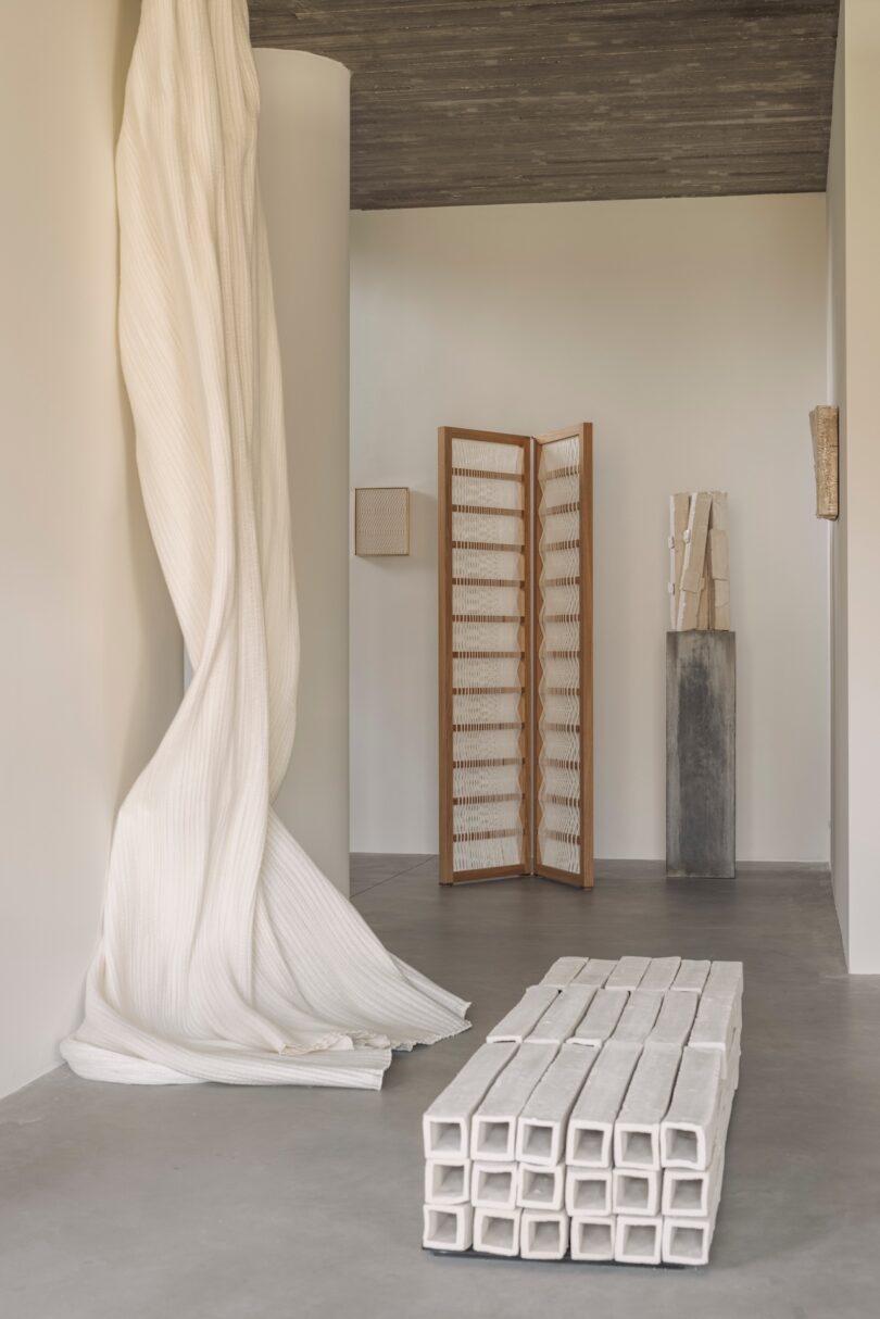 A minimalist room with draped fabrics, wooden screens, and various textured sculptures.