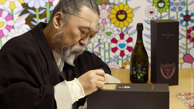 Takashi Murakami signing a black Dom Pérignon gift box at a table.
